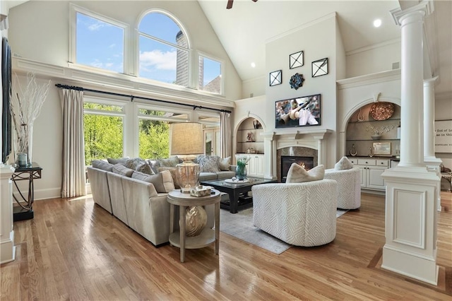 living room with a premium fireplace, light wood-style flooring, high vaulted ceiling, and ornate columns