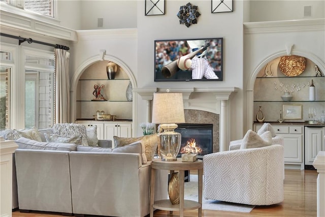 living room featuring a towering ceiling, wood finished floors, a glass covered fireplace, and plenty of natural light