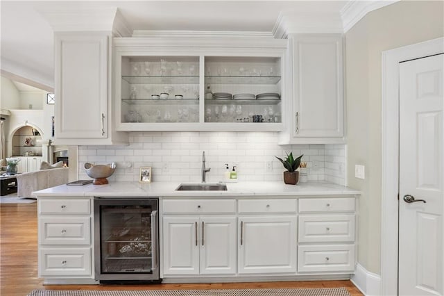 bar with backsplash, a sink, wine cooler, and light wood-style flooring