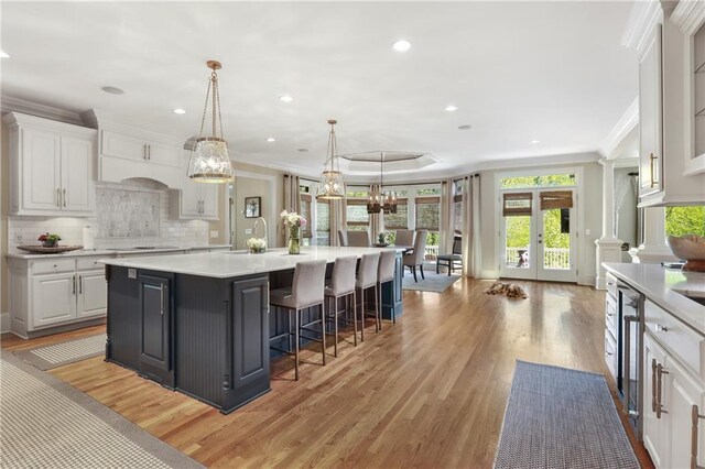 kitchen with white cabinets, light wood finished floors, a center island with sink, light countertops, and ornamental molding
