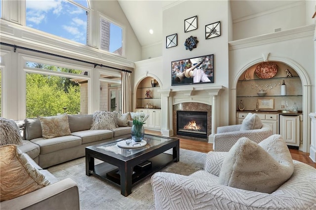 living room with a premium fireplace, wood finished floors, high vaulted ceiling, and built in shelves