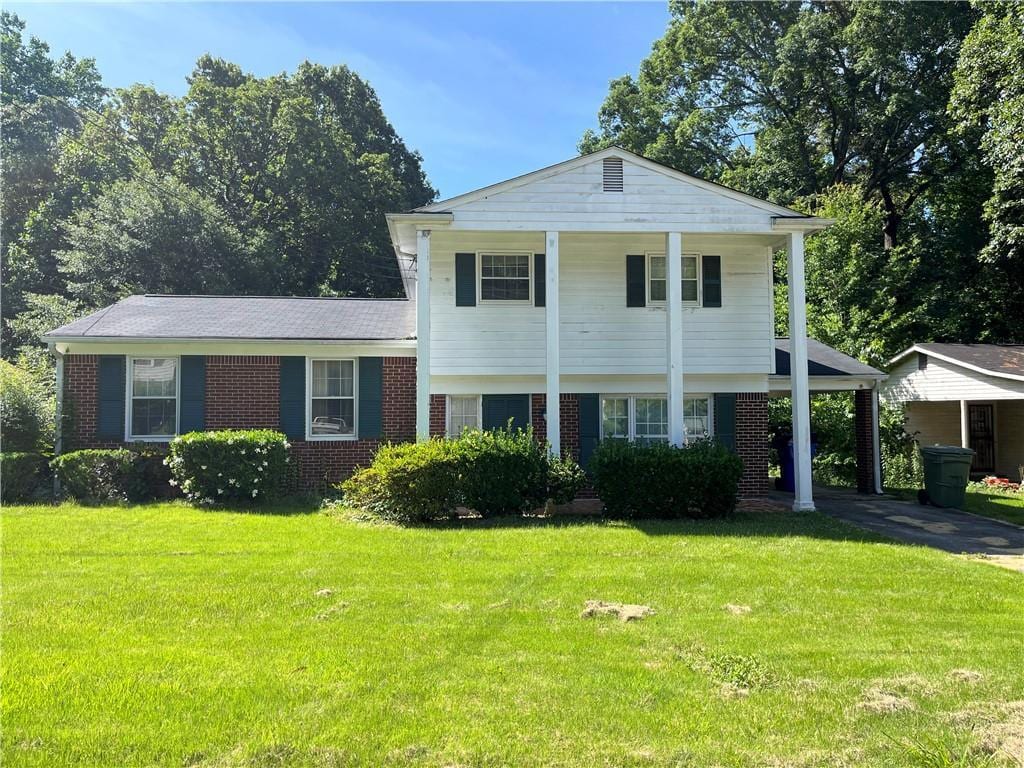 tri-level home featuring a front yard, an attached carport, concrete driveway, and brick siding