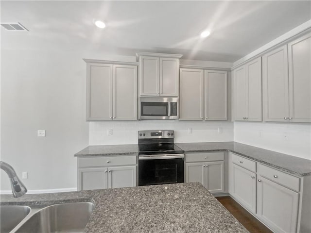 kitchen featuring gray cabinetry, sink, dark stone counters, and appliances with stainless steel finishes