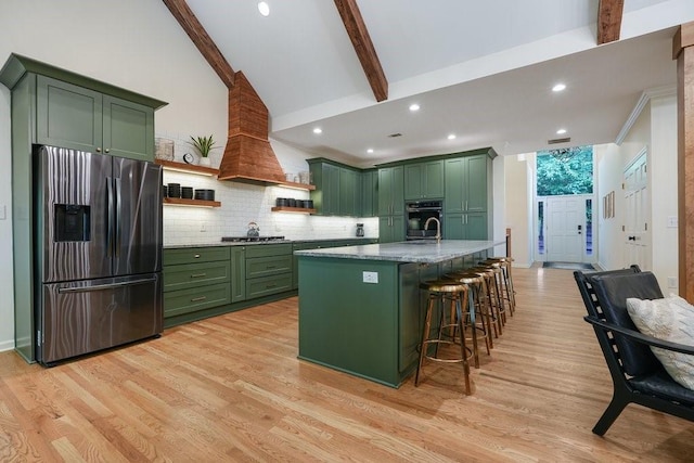 kitchen with stainless steel appliances, green cabinets, light hardwood / wood-style flooring, a breakfast bar area, and a kitchen island with sink