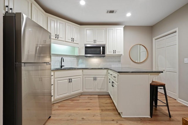 kitchen with white cabinetry, sink, kitchen peninsula, a kitchen bar, and appliances with stainless steel finishes