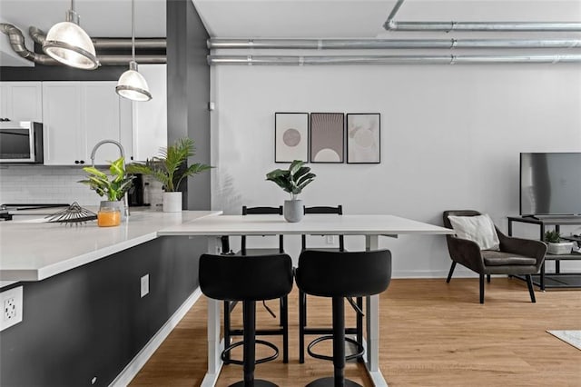 interior space with light hardwood / wood-style flooring, backsplash, a kitchen bar, pendant lighting, and white cabinetry