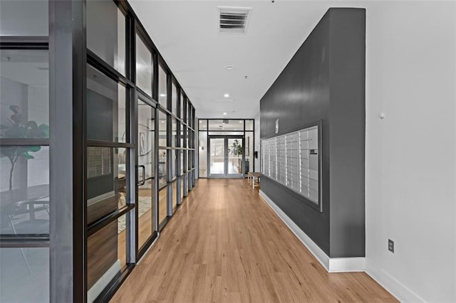 corridor with a wall of windows, light hardwood / wood-style flooring, and a mail area