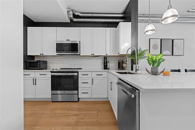 kitchen featuring appliances with stainless steel finishes, white cabinetry, sink, and hanging light fixtures