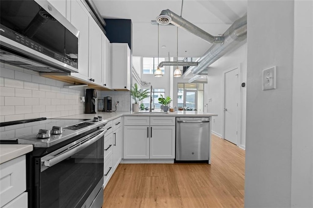 kitchen with white cabinets, hanging light fixtures, backsplash, appliances with stainless steel finishes, and light hardwood / wood-style floors