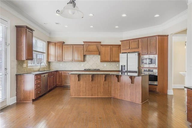 kitchen with premium range hood, dark wood-style flooring, a center island, appliances with stainless steel finishes, and brown cabinets