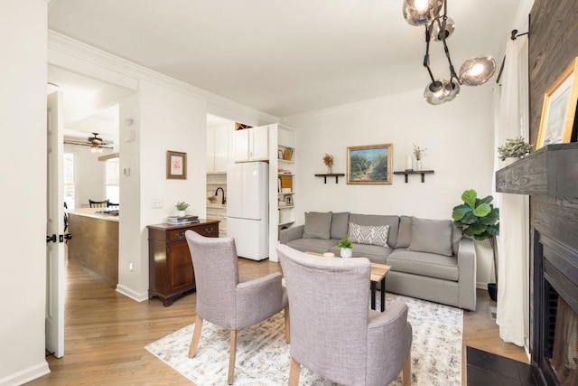 living area with crown molding, baseboards, a fireplace with flush hearth, light wood-type flooring, and a ceiling fan