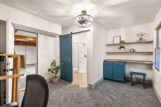 office area with a barn door, baseboards, and dark carpet