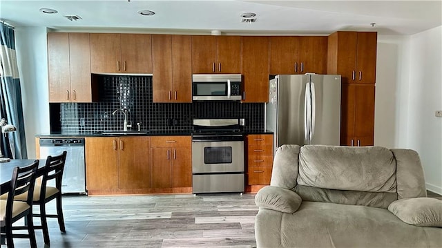 kitchen featuring stainless steel appliances, a sink, light wood-style floors, open floor plan, and dark countertops