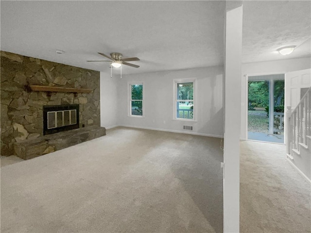 unfurnished living room with a fireplace, a textured ceiling, light colored carpet, and ceiling fan