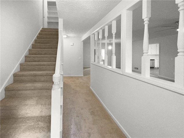 stairway with carpet flooring, ceiling fan, and a textured ceiling