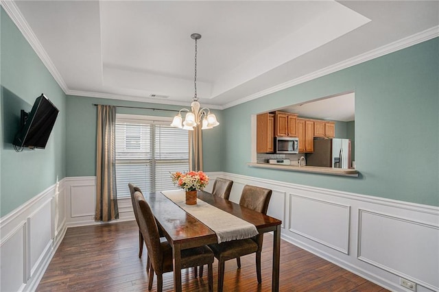 dining area with a raised ceiling, a decorative wall, a chandelier, and dark wood finished floors