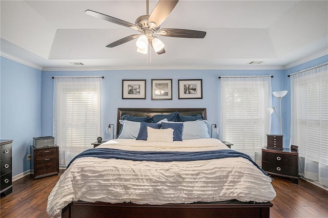 bedroom featuring a raised ceiling, dark wood-style flooring, and multiple windows