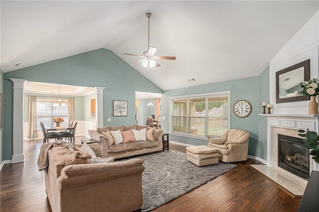 living area with ornate columns, ceiling fan with notable chandelier, wood finished floors, and a premium fireplace