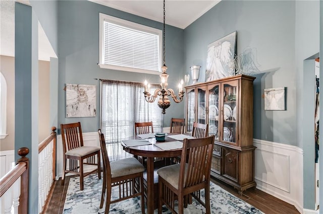 dining room featuring a notable chandelier, a decorative wall, a high ceiling, dark wood-type flooring, and wainscoting