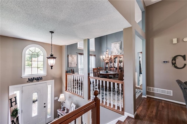 foyer with a notable chandelier, visible vents, a textured ceiling, wood finished floors, and baseboards