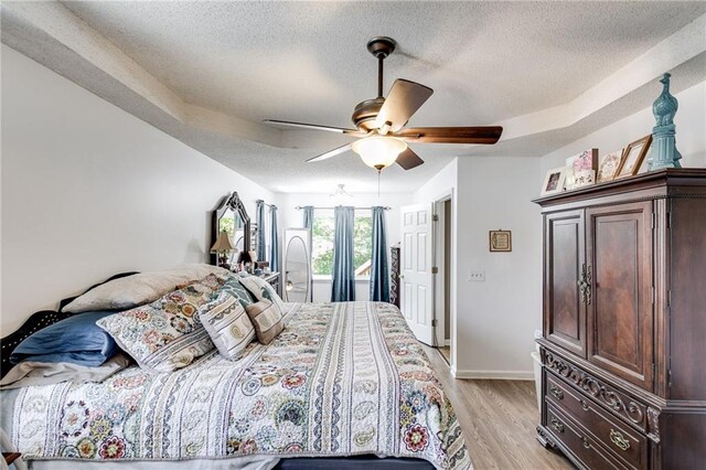 bedroom featuring a textured ceiling, light wood-type flooring, a ceiling fan, and baseboards