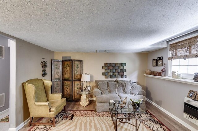 living area with heating unit, visible vents, a textured ceiling, wood finished floors, and baseboards