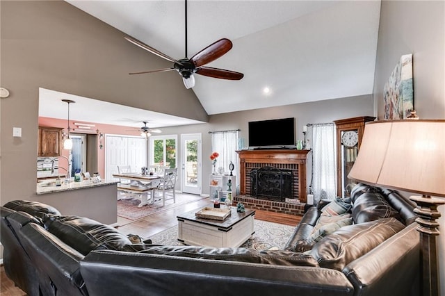 living room with high vaulted ceiling, a fireplace, ceiling fan, and light hardwood / wood-style flooring