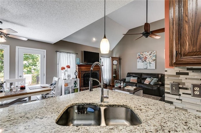 kitchen featuring light stone counters, a ceiling fan, open floor plan, and a sink