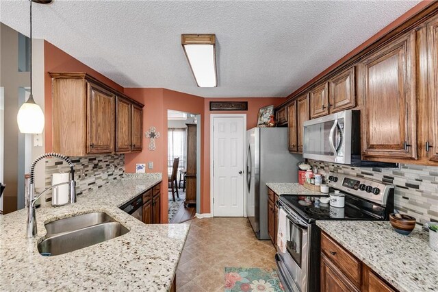 kitchen with appliances with stainless steel finishes, decorative backsplash, a sink, and light stone countertops