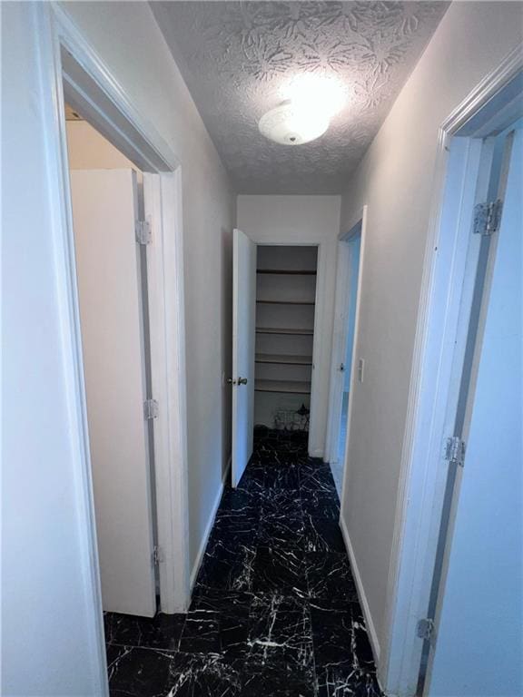 hallway featuring a textured ceiling, marble finish floor, and baseboards