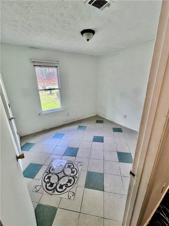 empty room with tile patterned flooring, visible vents, and a textured ceiling