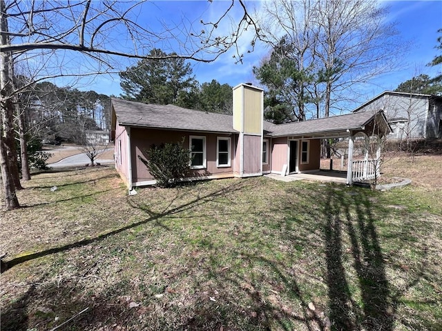 rear view of house featuring a chimney and a lawn