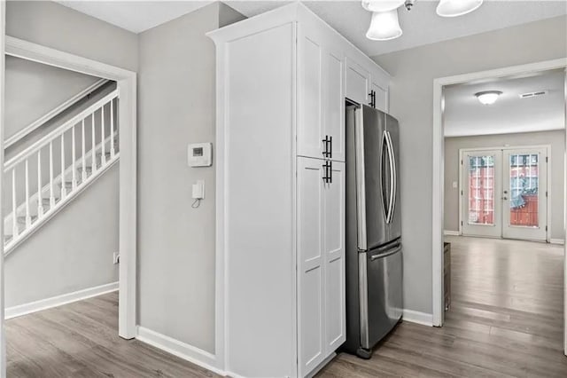 kitchen with stainless steel refrigerator, white cabinetry, light hardwood / wood-style flooring, and french doors