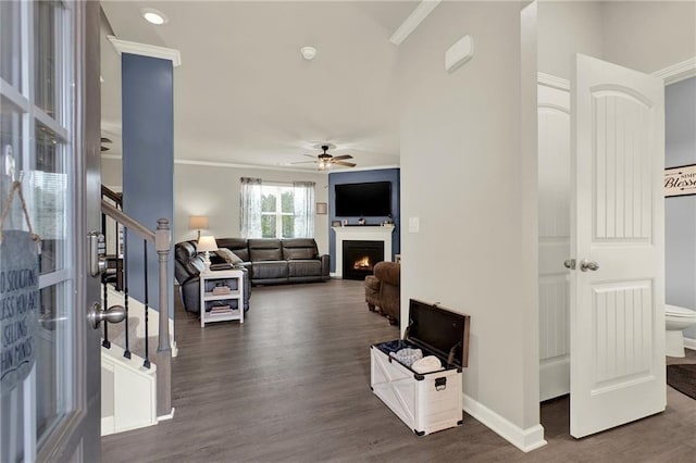 living room featuring baseboards, a ceiling fan, dark wood-style flooring, a lit fireplace, and stairs