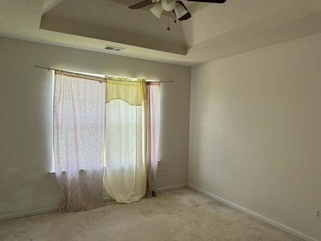 carpeted spare room with a textured ceiling, ceiling fan, and a raised ceiling