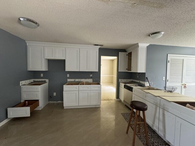 kitchen with white cabinets, white dishwasher, light tile patterned floors, and a textured ceiling