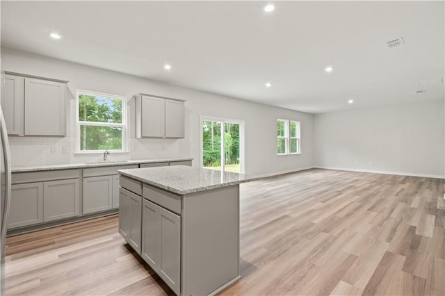 kitchen featuring light wood-type flooring, gray cabinetry, a kitchen island, and light stone countertops