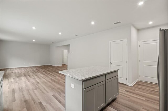 kitchen featuring stainless steel fridge, a center island, light hardwood / wood-style floors, and light stone countertops