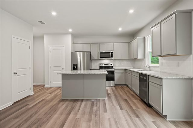 kitchen featuring light hardwood / wood-style flooring, stainless steel appliances, light stone counters, a center island, and gray cabinetry