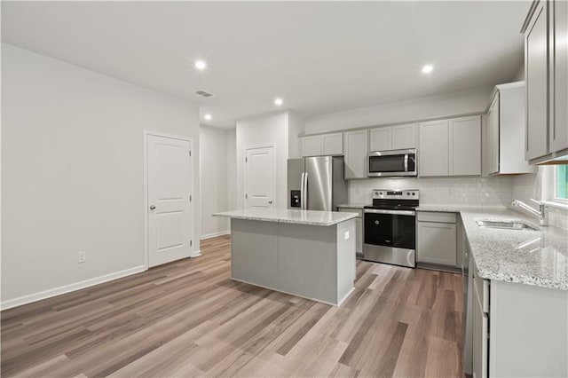 kitchen featuring a center island, light wood-type flooring, appliances with stainless steel finishes, sink, and gray cabinets