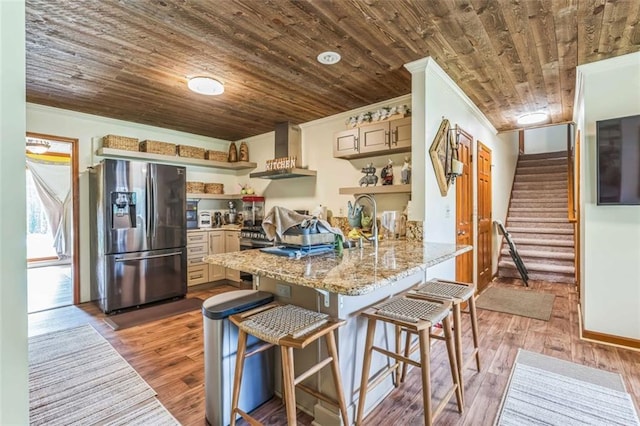kitchen featuring stainless steel refrigerator with ice dispenser, open shelves, a peninsula, ornamental molding, and wall chimney exhaust hood