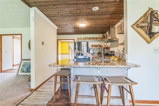 kitchen with a peninsula, baseboards, a kitchen breakfast bar, wall chimney range hood, and light stone counters