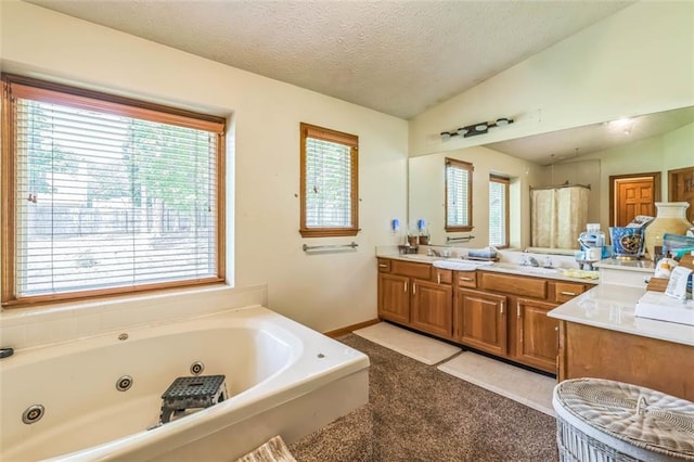 full bath with vanity, a textured ceiling, vaulted ceiling, and a jetted tub