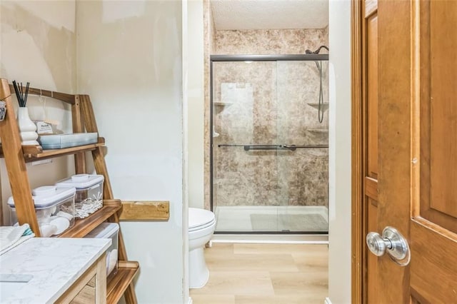 full bath with a textured ceiling, a stall shower, toilet, and wood finished floors