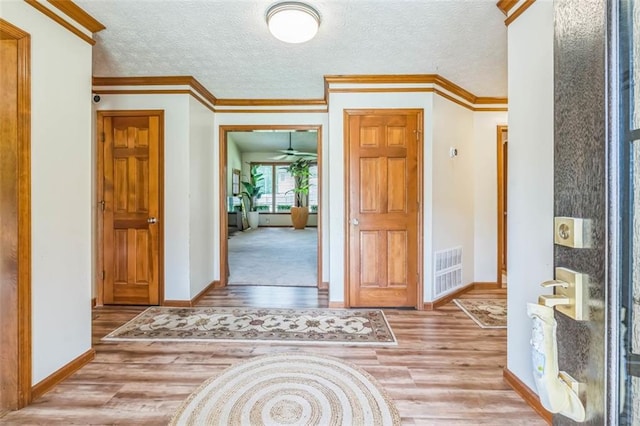 foyer entrance featuring a textured ceiling, baseboards, wood finished floors, visible vents, and ornamental molding