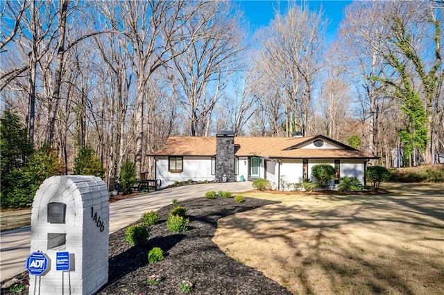 ranch-style house with a chimney, a front lawn, and curved driveway