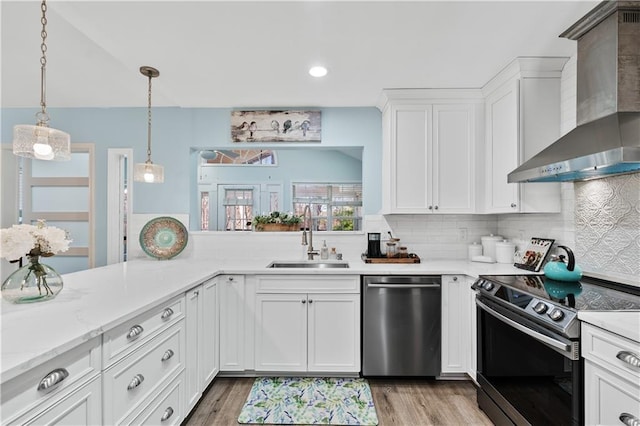 kitchen with decorative backsplash, a sink, wall chimney range hood, white cabinets, and appliances with stainless steel finishes