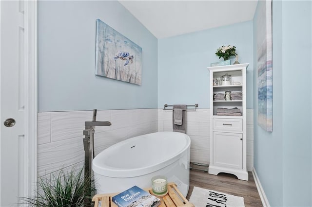 full bath with tile walls, wood finished floors, a soaking tub, and wainscoting