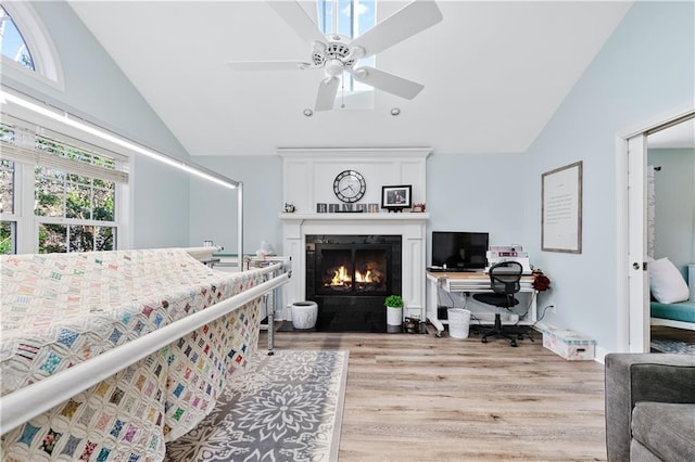 bedroom featuring a ceiling fan, a fireplace with flush hearth, lofted ceiling, and light wood-type flooring
