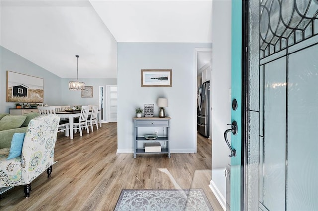 entrance foyer featuring baseboards, vaulted ceiling, wood finished floors, and an inviting chandelier